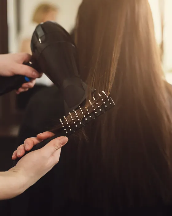 Client's hair being blow-dried and smoothed with a round brush.