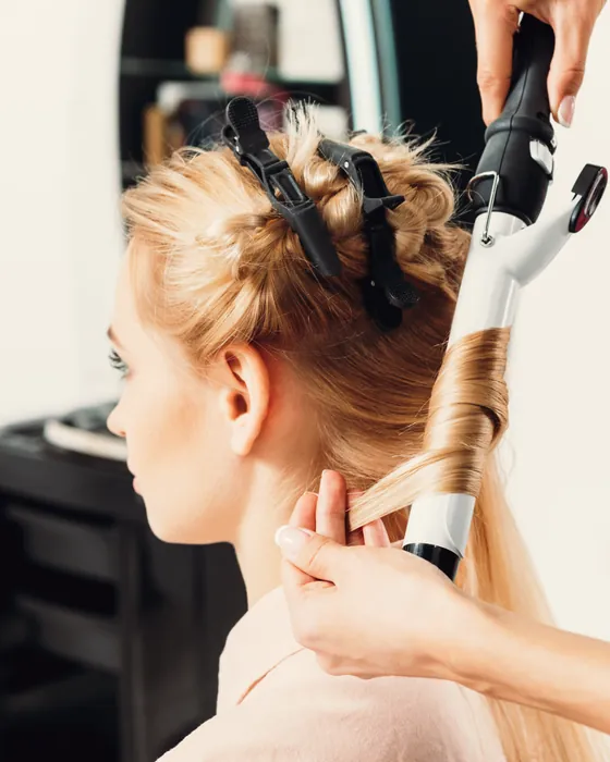 Stylist curling a section of a client's hair with a wand.