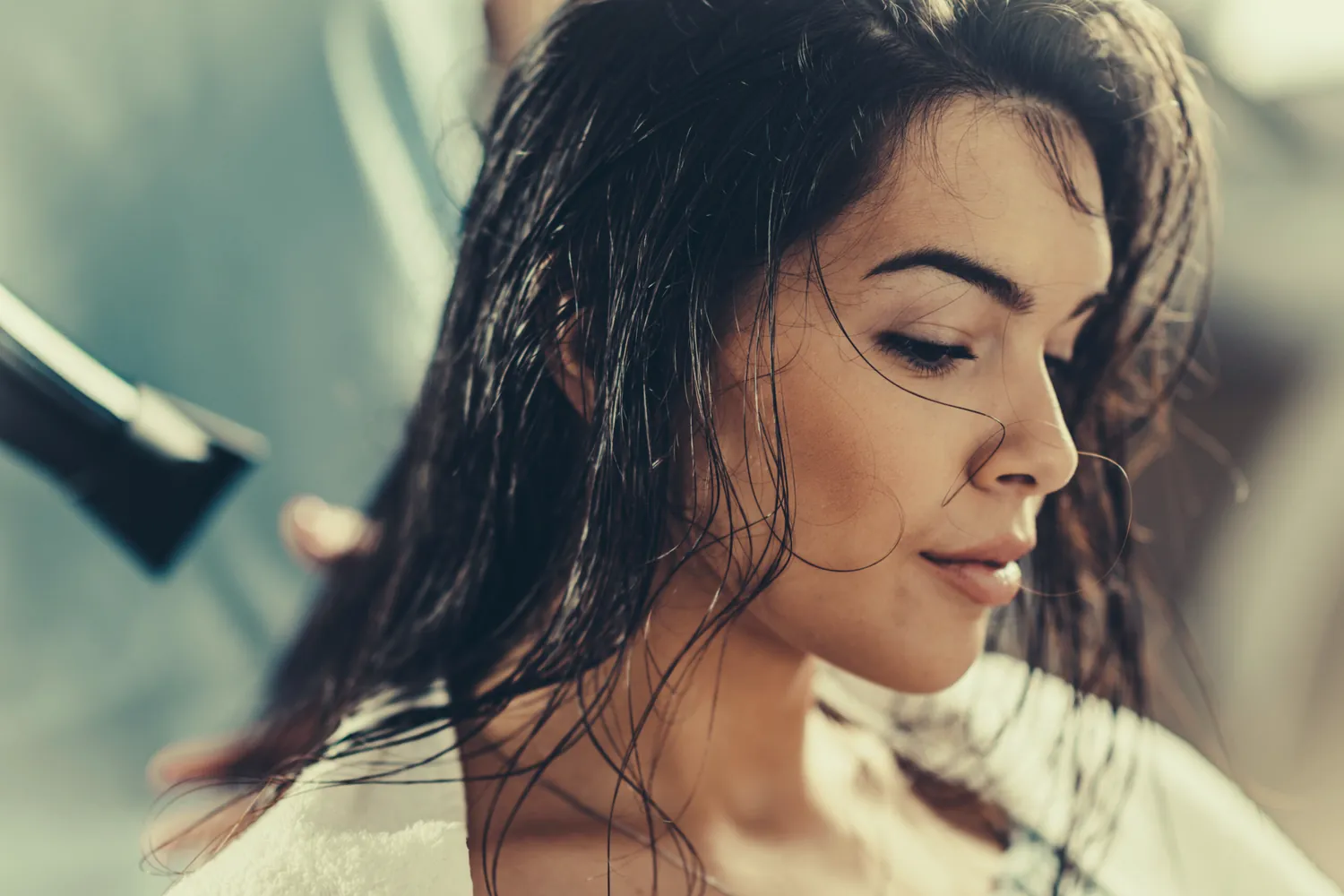 Stylist blow-drying a client&rsquo;s long dark hair.