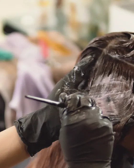 Gloved hands working tint through sectioned hair with a tail comb.