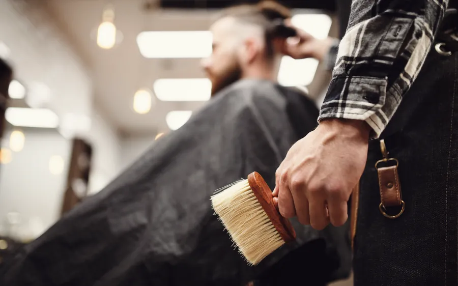 Barber holding a neck brush beside a client mid-haircut.