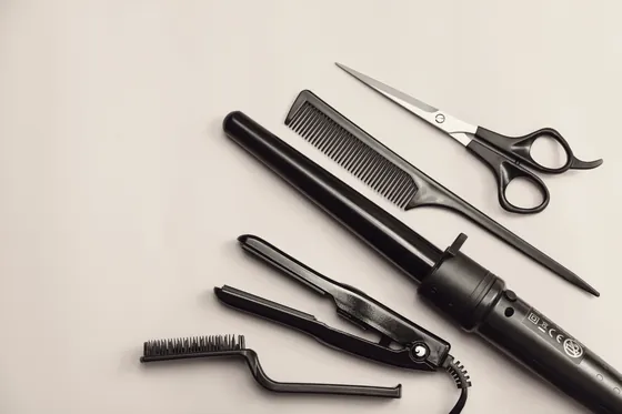Shears, tail comb, flat iron and curling wand laid out on a plain surface.