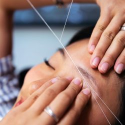 detail of an eyebrow waxing with threading on a young woman in a beauty salon, concept of wellness and body care