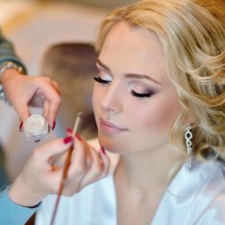 Wedding makeup artist making a make up for bride. Beautiful sexy model girl indoors. Beauty woman with curly hair. Female portrait. Bridal morning of a cute lady. Close-up hands near face