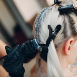 Young woman hairdresser dying hair at beauty salon. Professional hair roots coloring.